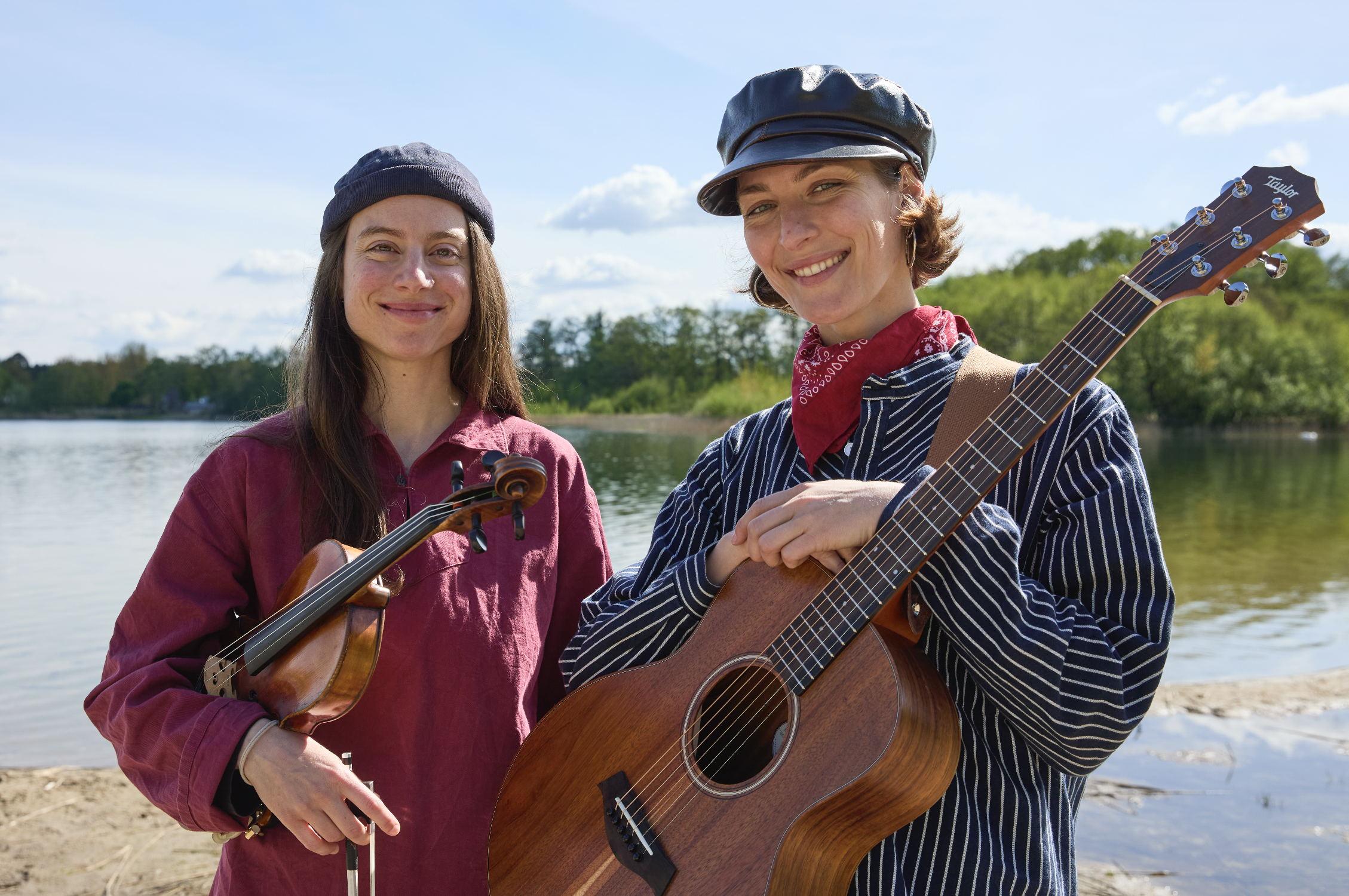 Zwei Frauen mit Gitarre und Geige stehen vor einem Strand an am Meer